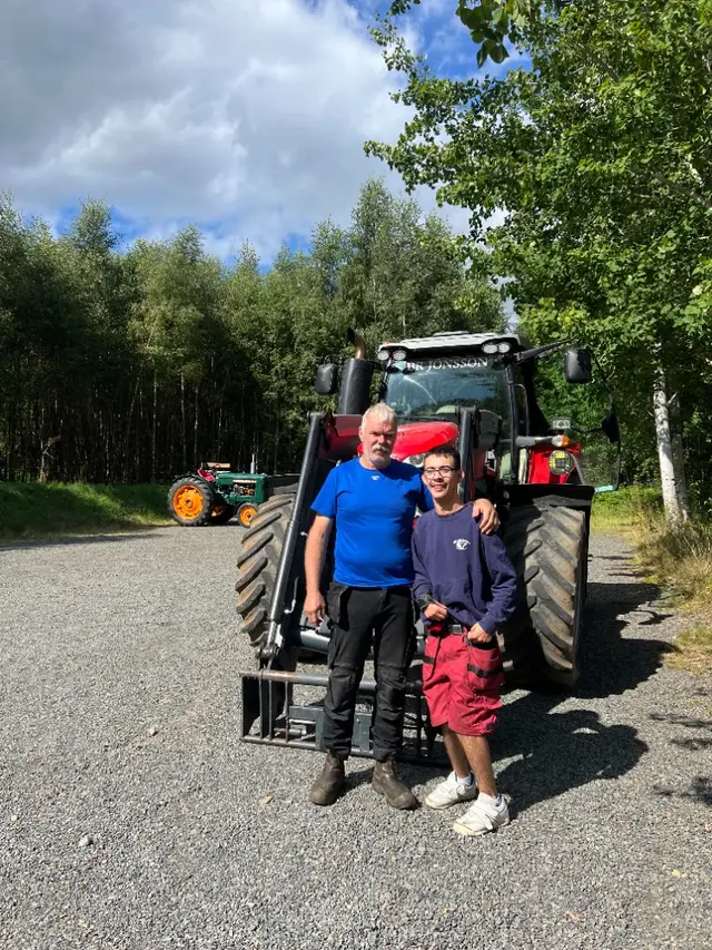 Två personer framför en röd traktor