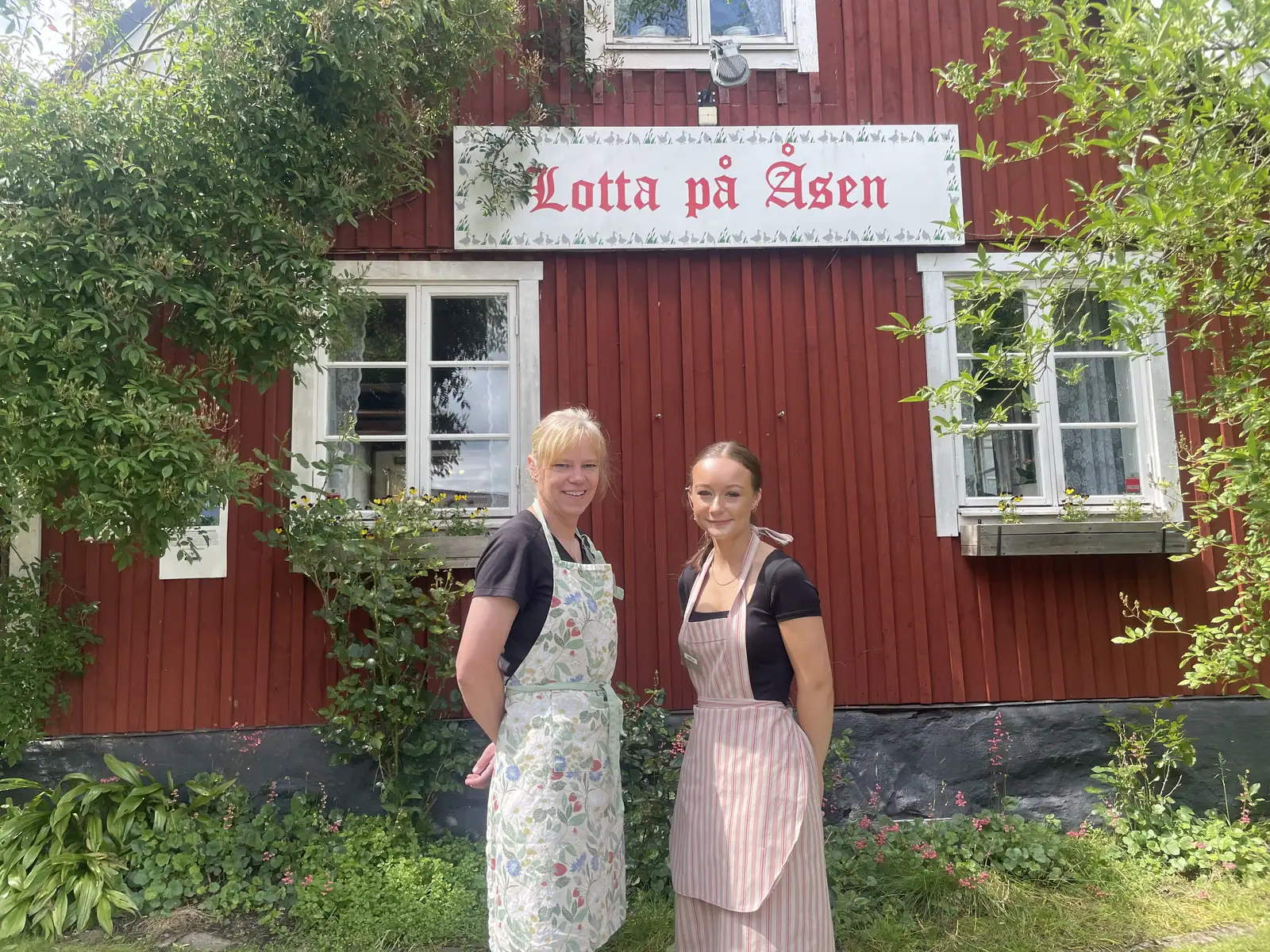 Marika och Amelia framför det röda caféhuset med skylten Lotta på Åsen