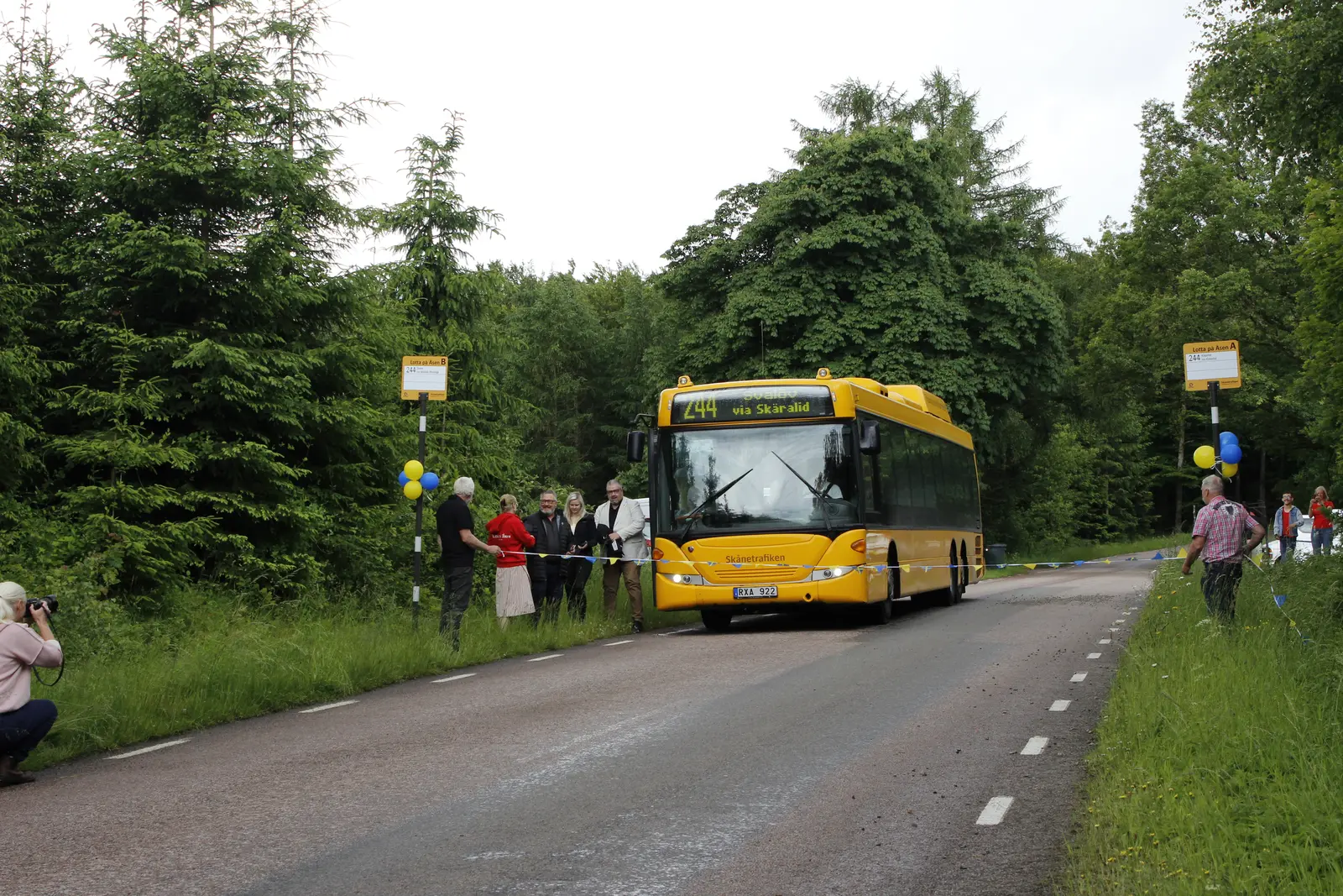 Skånetrafikens gula regionbuss vid hållplatsen, med resenärer längs vägen