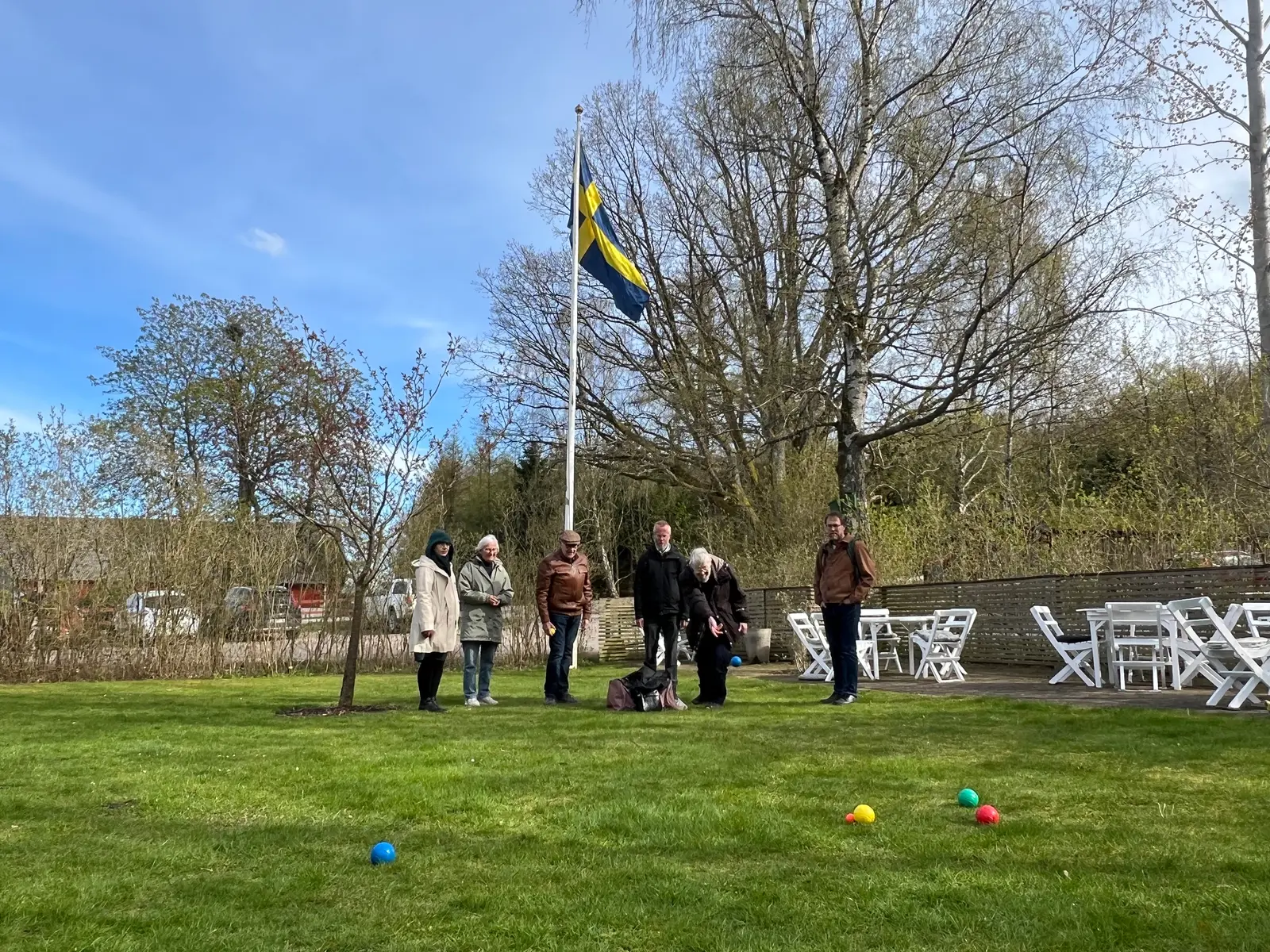Sällskap spelar boule på gräsmattan vid flaggstången